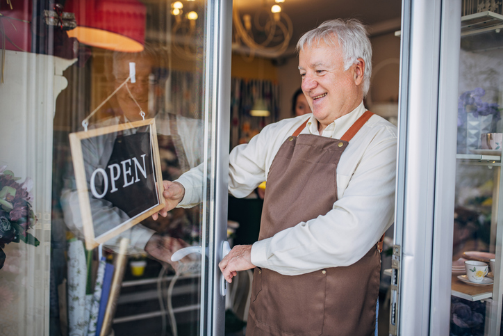 Elderly shopkeeper opening store with a smile on face.